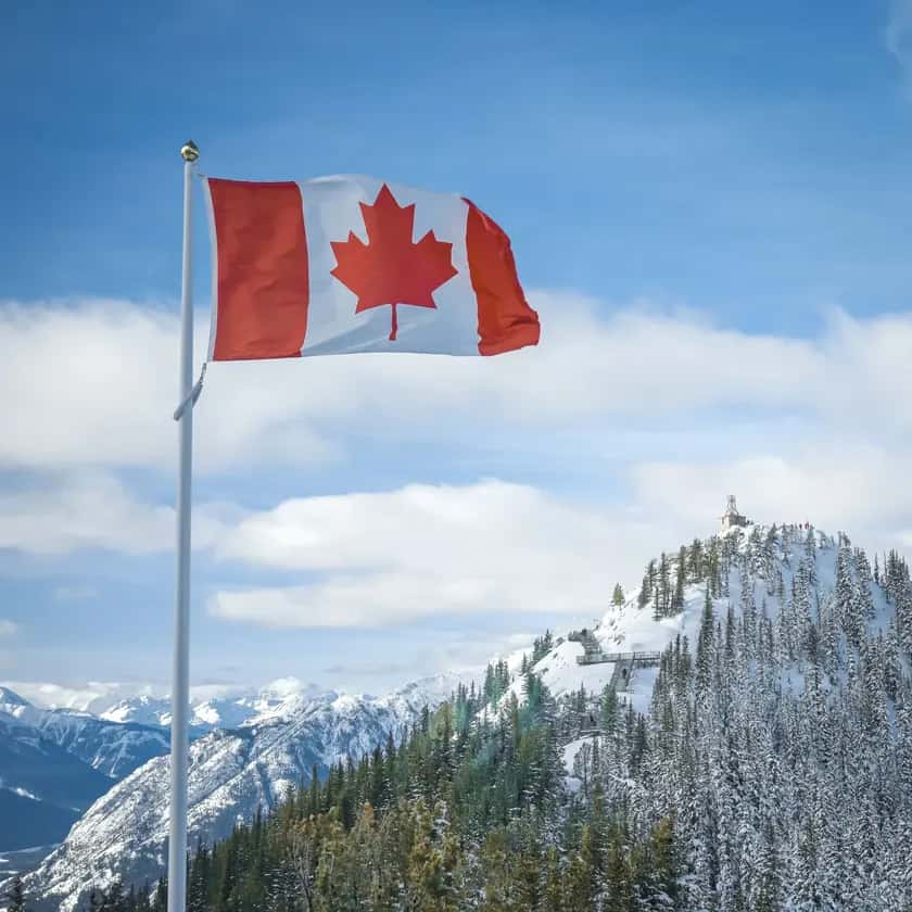 Canadian flag flying over snowy mountains.